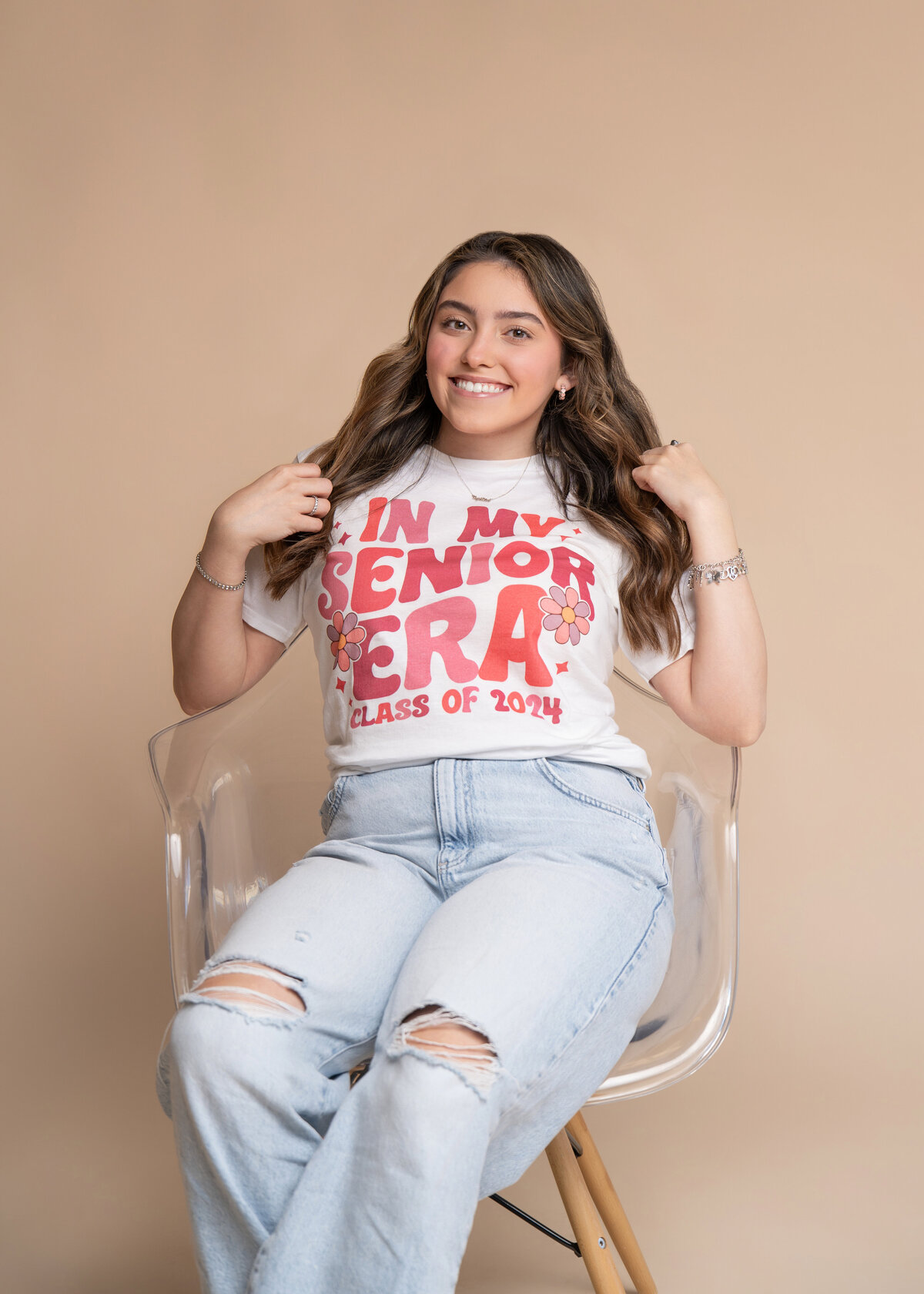 High School senior sitting in a clear chair smiles for her senior picture