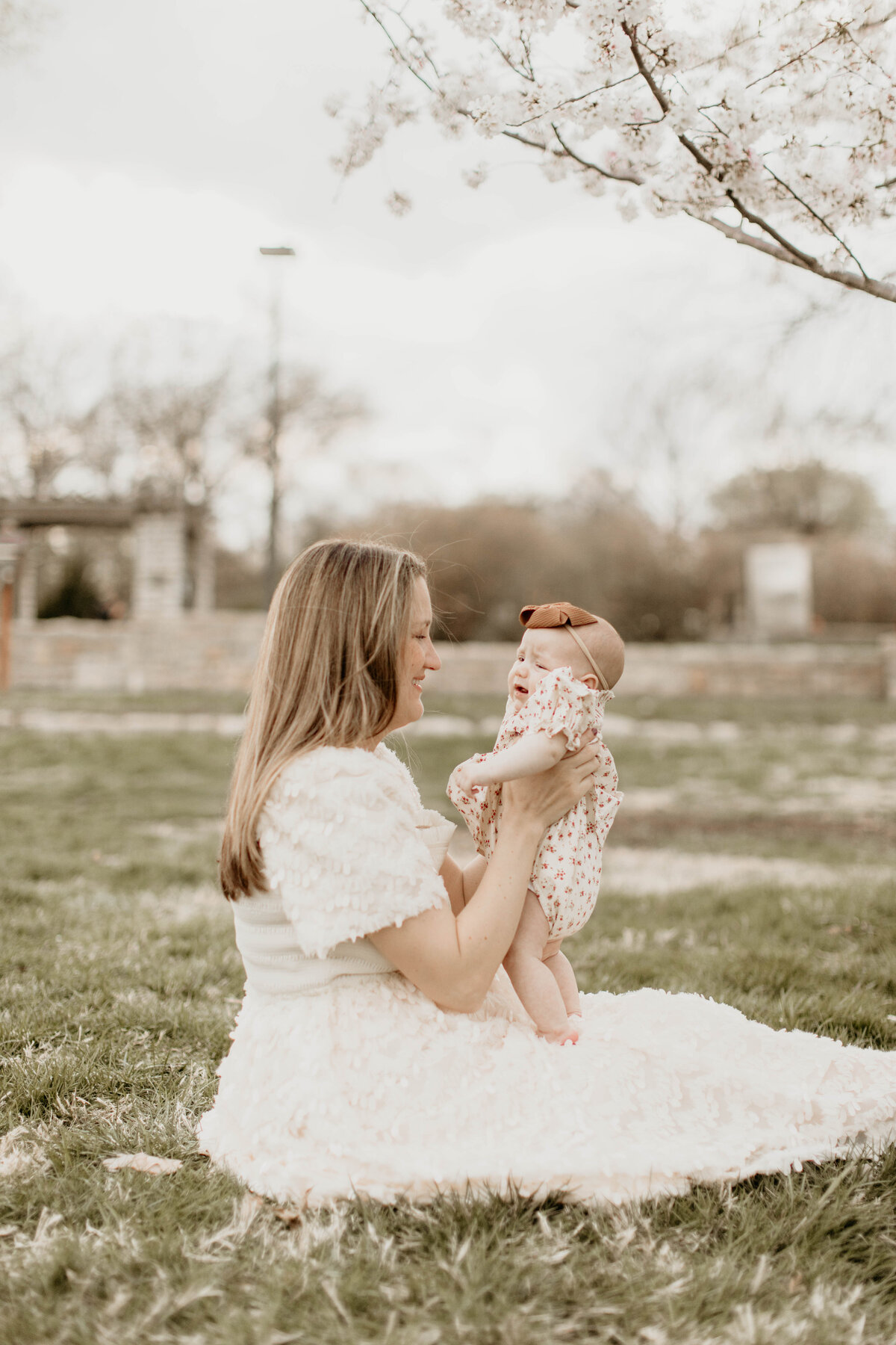 Mom holding youngest baby at the park under a blooming tree.
