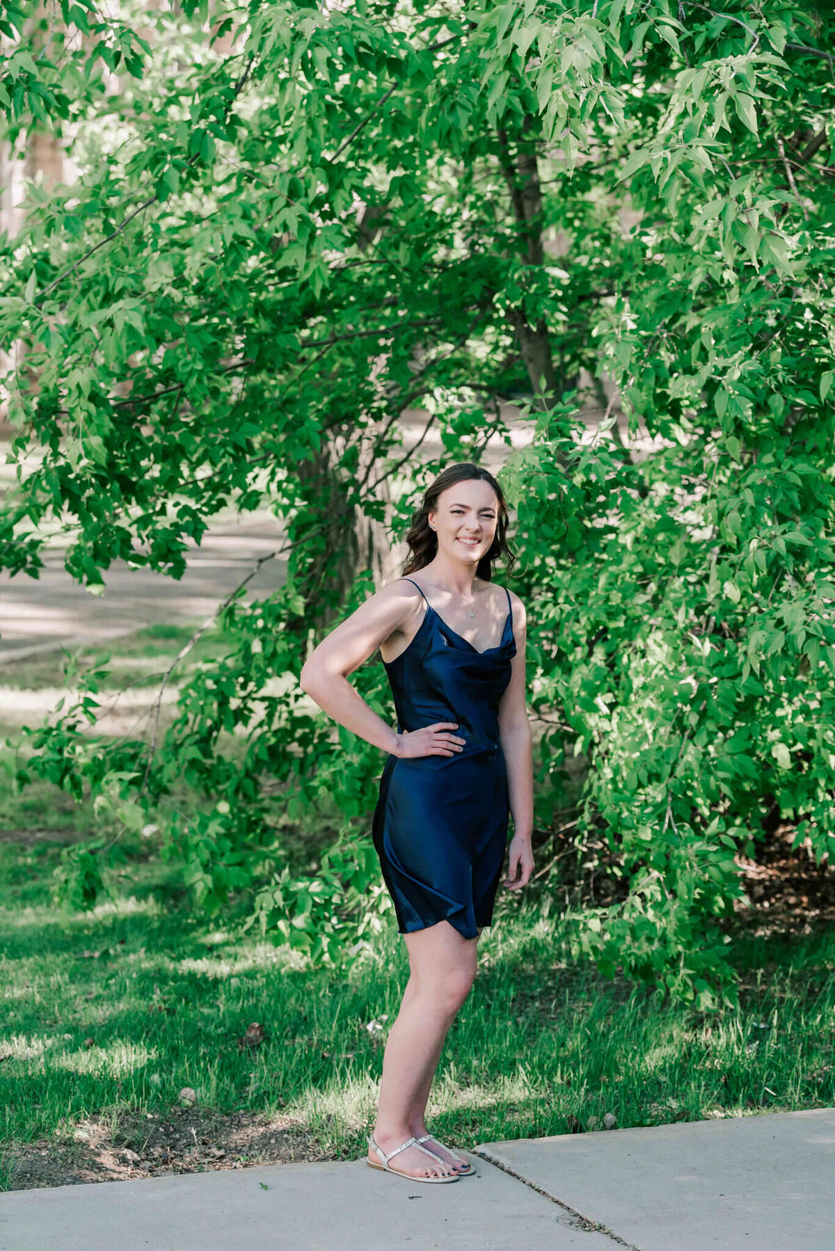 A young lady standing in front of trees with her hand on her hip. 