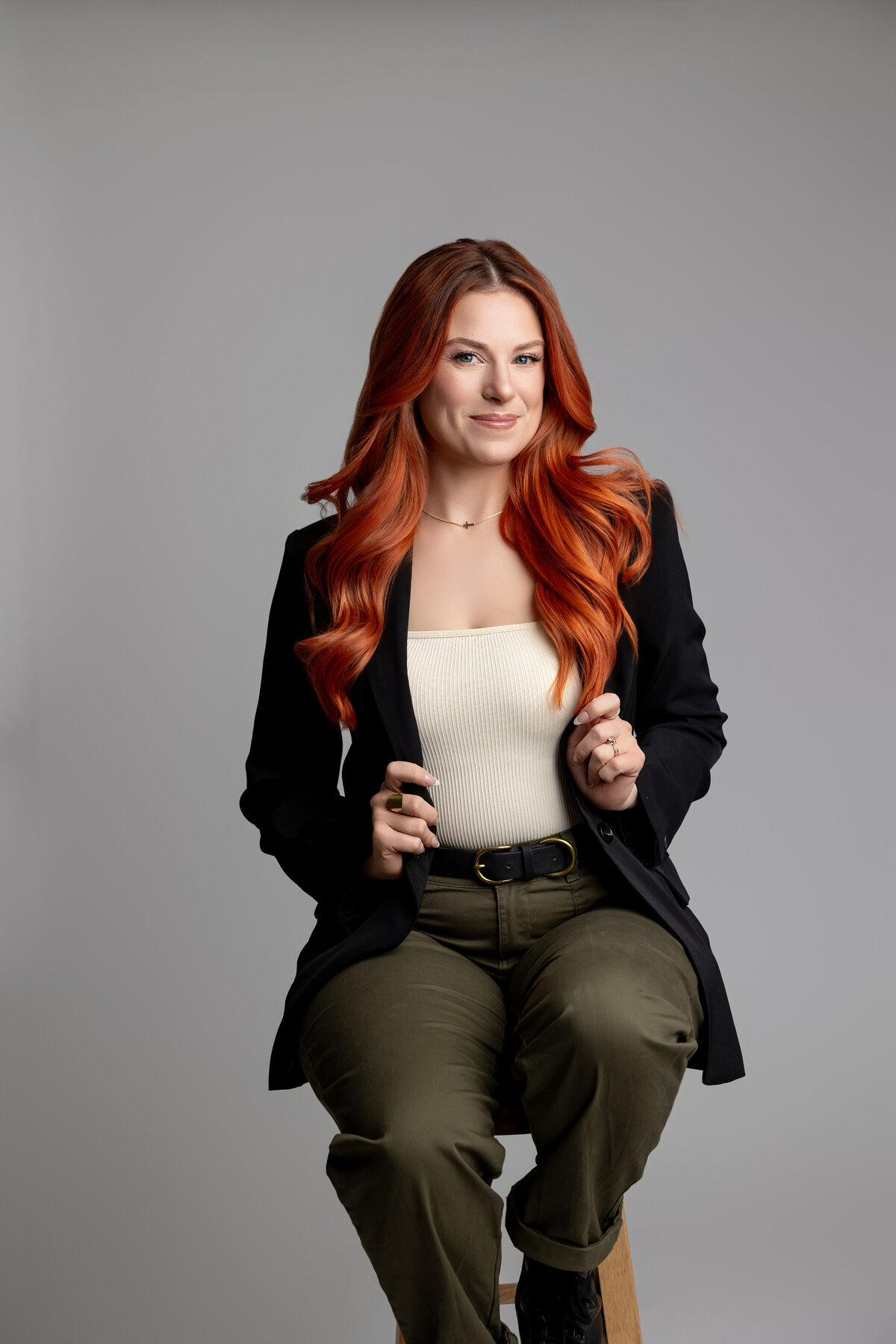 Professional woman with red hair standing with hands on waist, smiling in studio. Photograph by Yucaipa branding photographer Kaitlyn Dawn Photography.