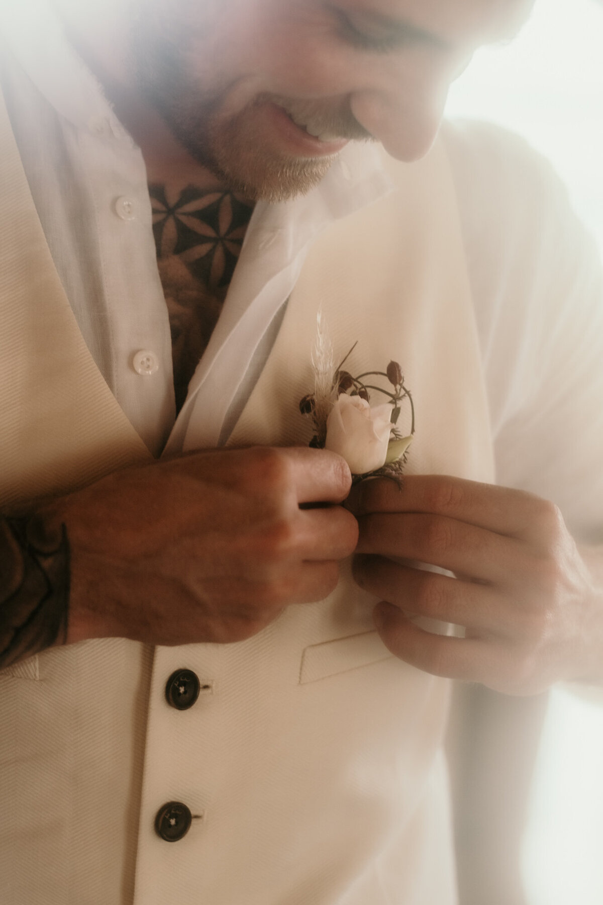 Mit beiden Händen befestigt der Bräutigam eine weiße Ansteckblume an seiner Weste.