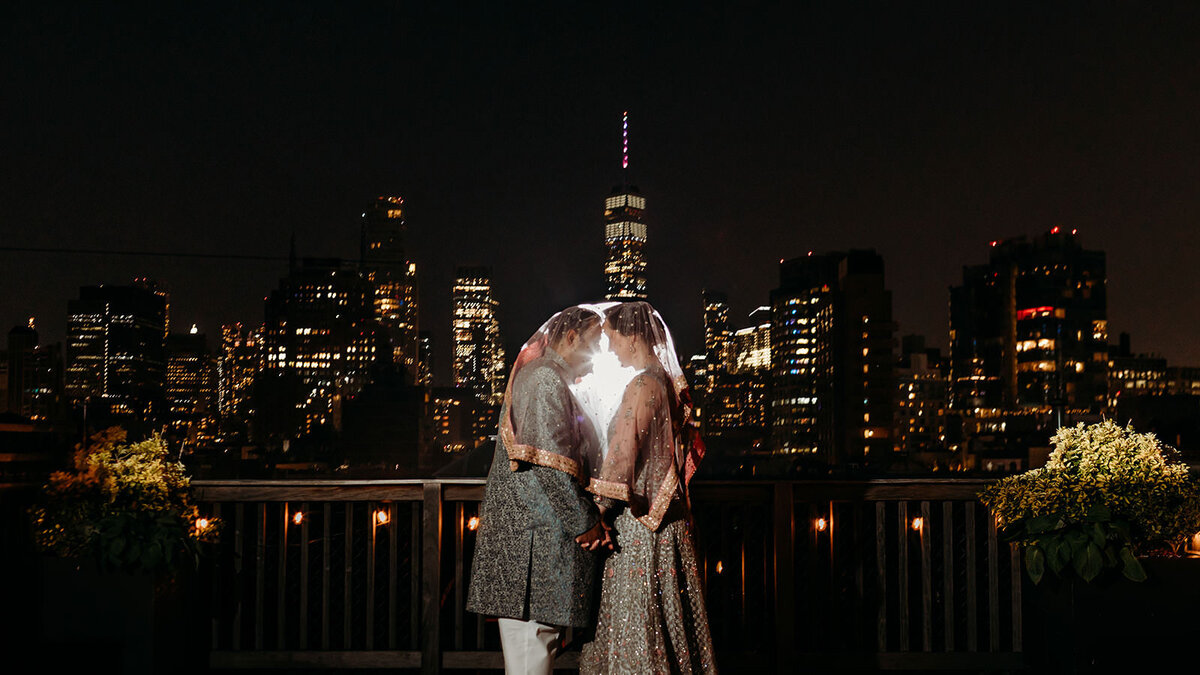 Bride and groom embrace underneath a veil with NYC skyline in the background