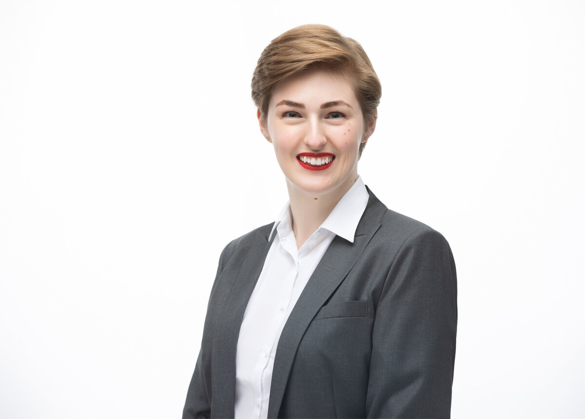 An executive businesswoman with short brown hair wearing a grey jacket with red lipstick poses for a professional headshot on a white background for Janel Lee Photography studios Cincinnati Ohio