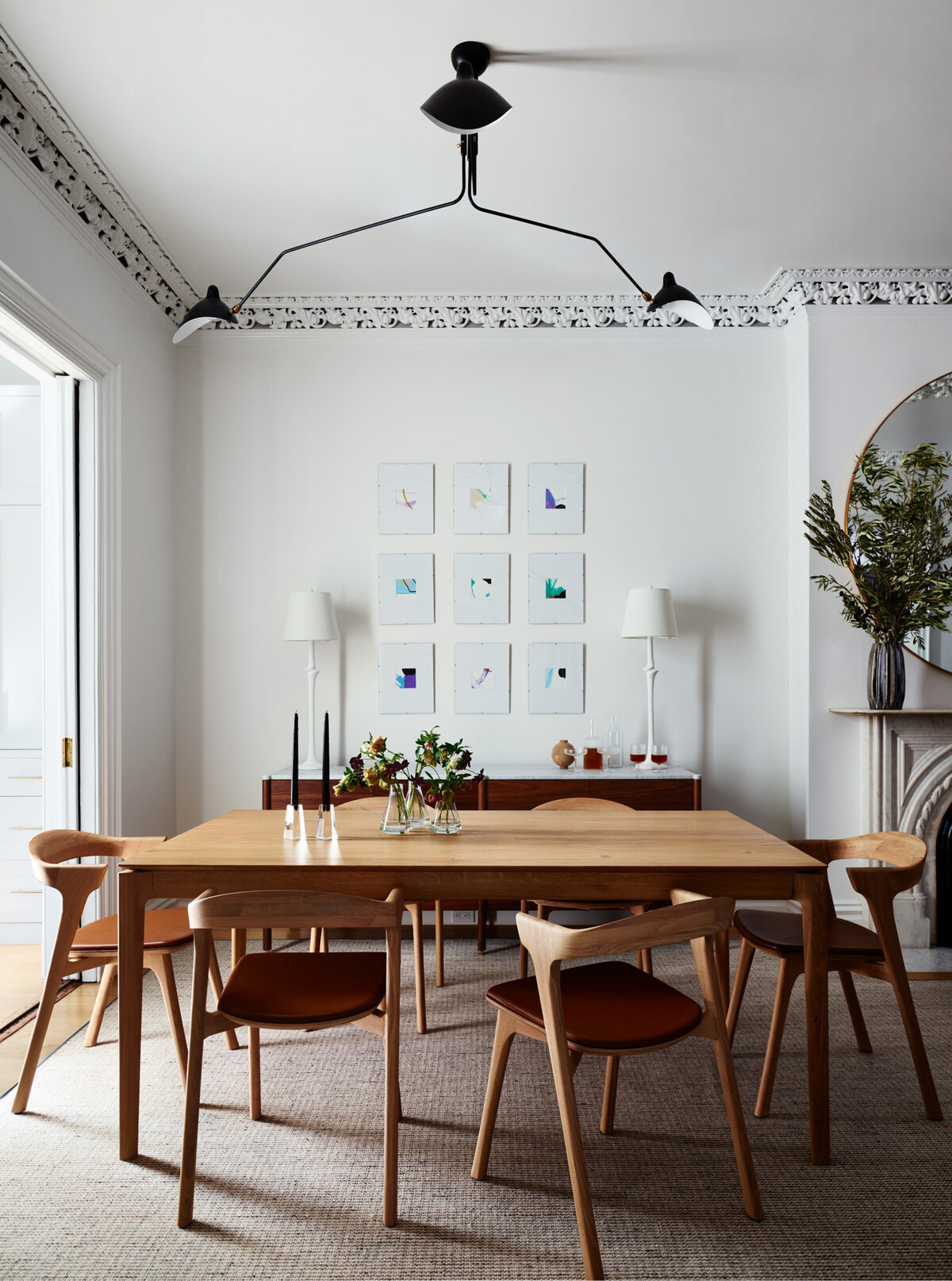 Sarah Scales Design Studio, Boston, features clean white gallery walls, neutral-toned art, and angled details on dining chairs in this mid-century inspired dining room