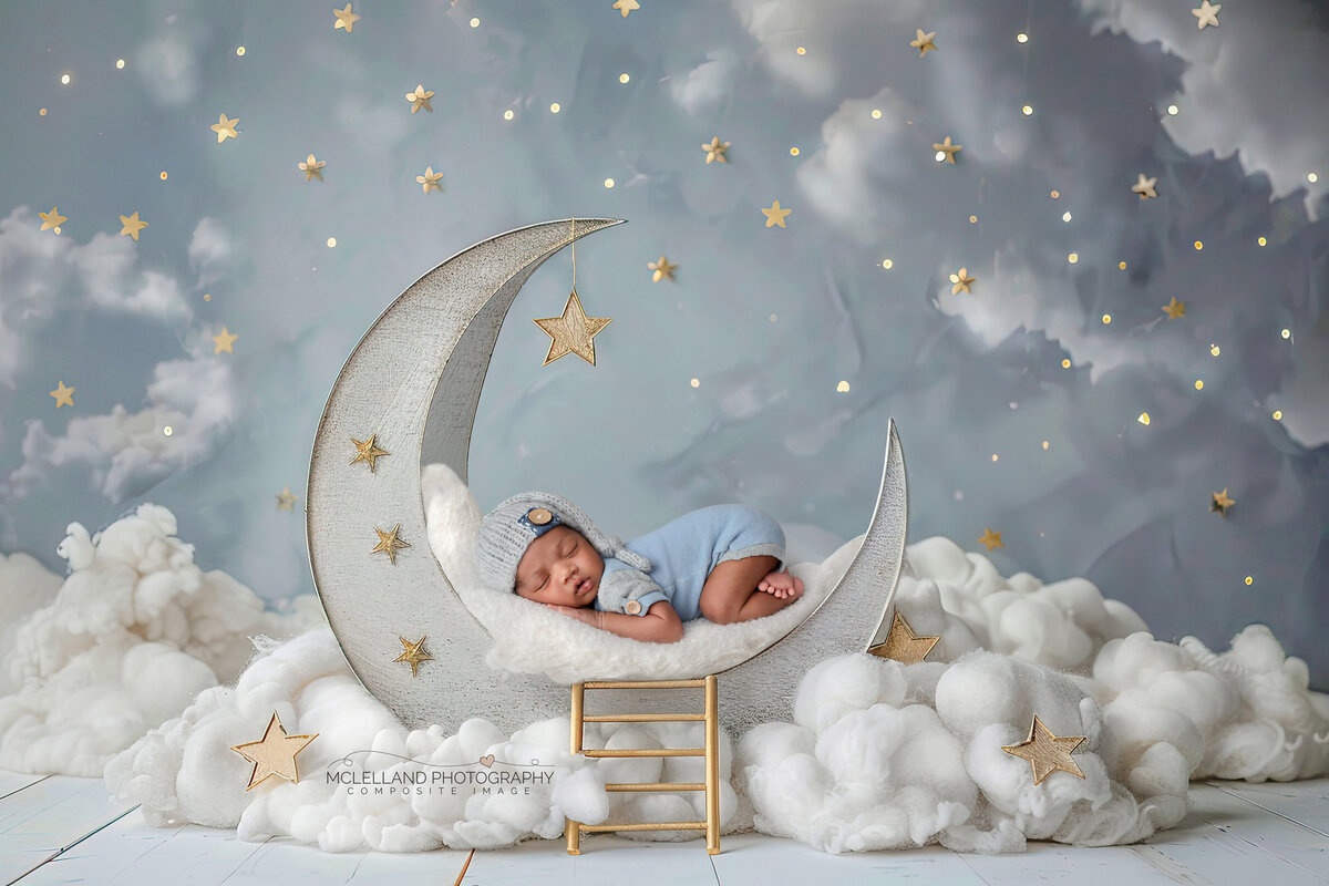 Newborn boy sleeping on a crescent moon prop with clouds and golden stars.