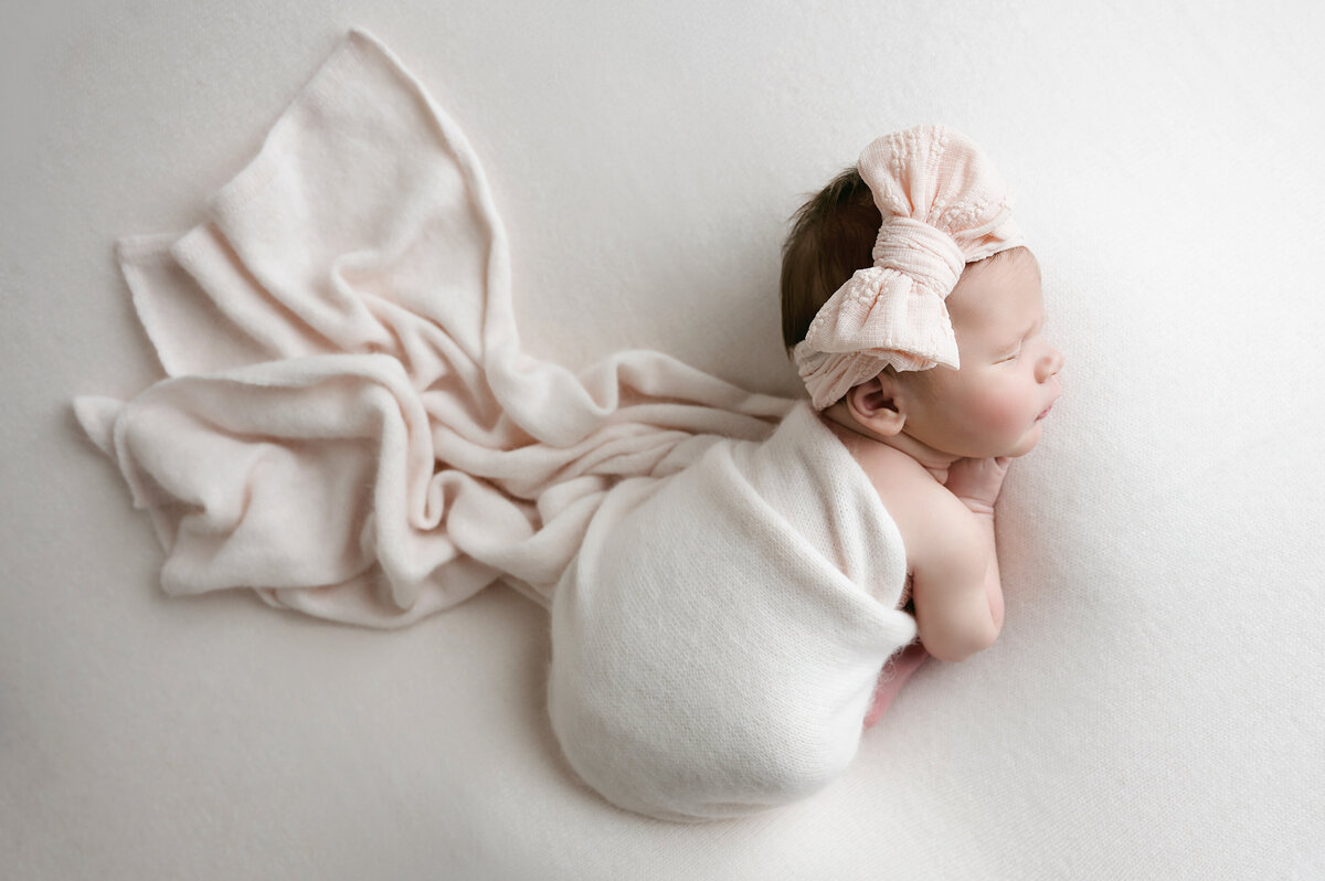 This serene newborn baby portrait captures a peaceful moment during a photoshoot in Pittsburgh, PA. Wrapped in a soft, light pink blanket and wearing an adorable bow headband, this image highlights the beauty and innocence of a newborn’s first days. Perfect for expecting moms seeking timeless newborn photography.