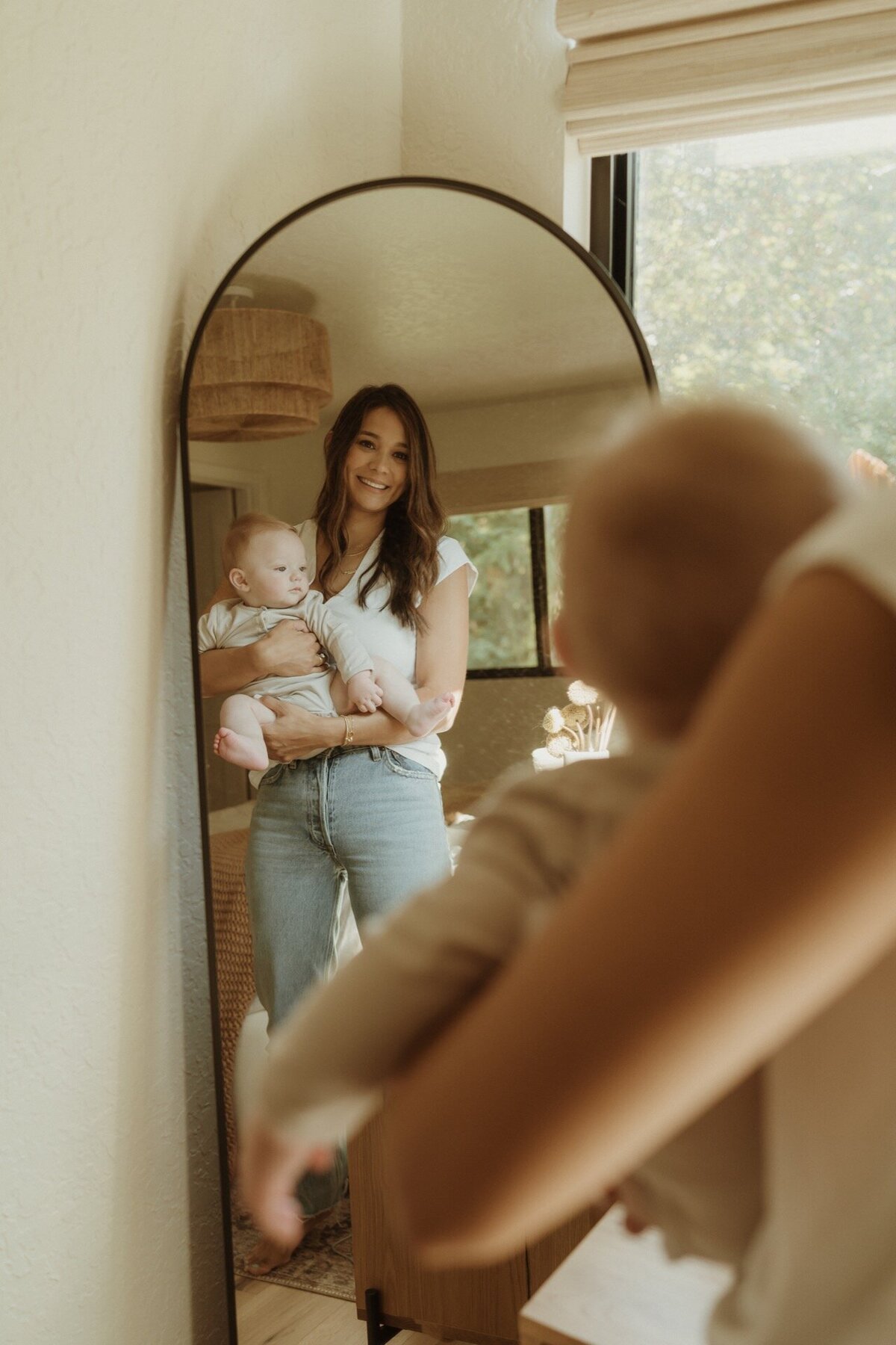mother holding newborn baby in mirror at home