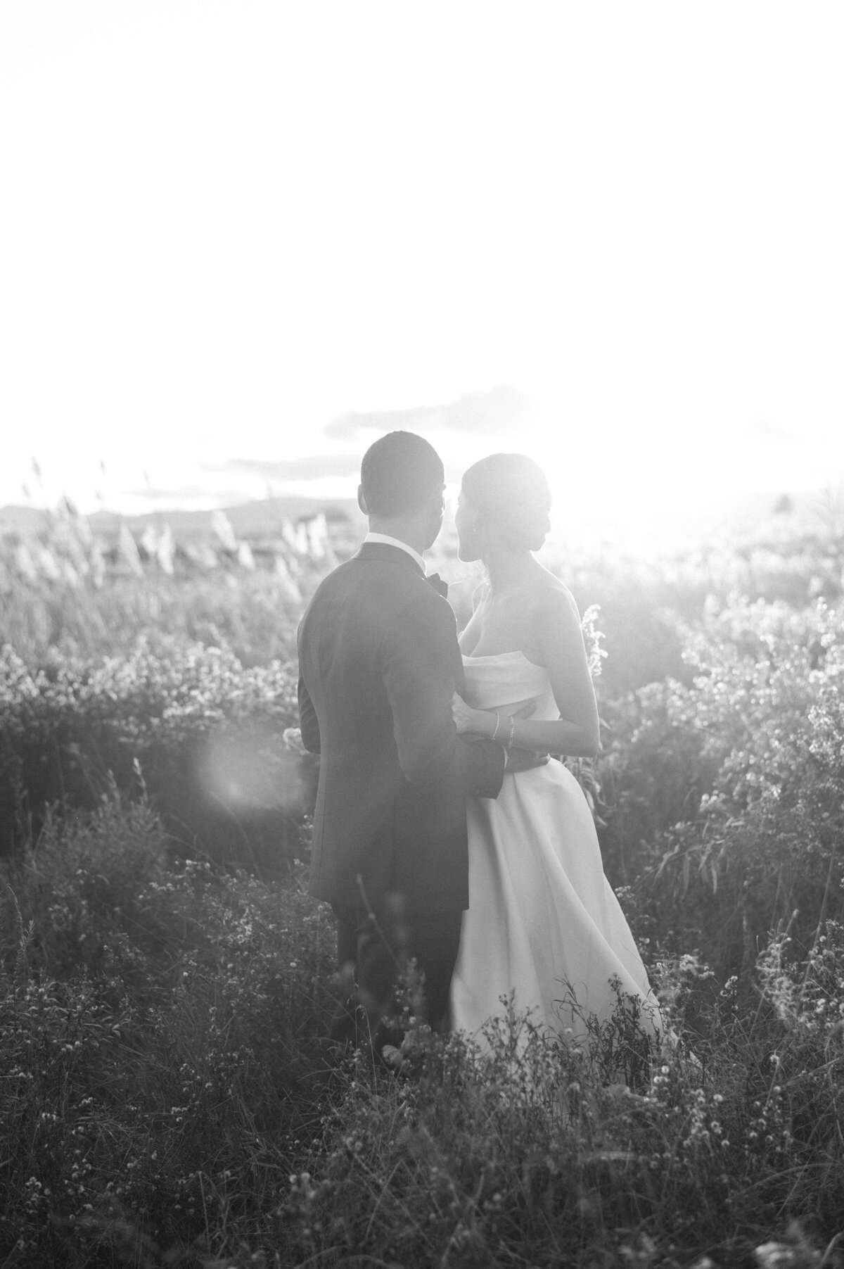 the couple embracing as they watch the sunset over the open fields