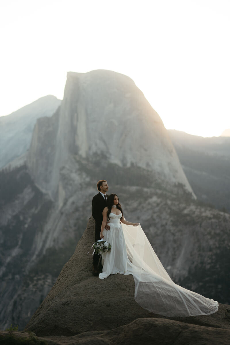 Glacier Point Wedding: Bride tosses her dress in the wind standing as her and groom stare of into the distance. 