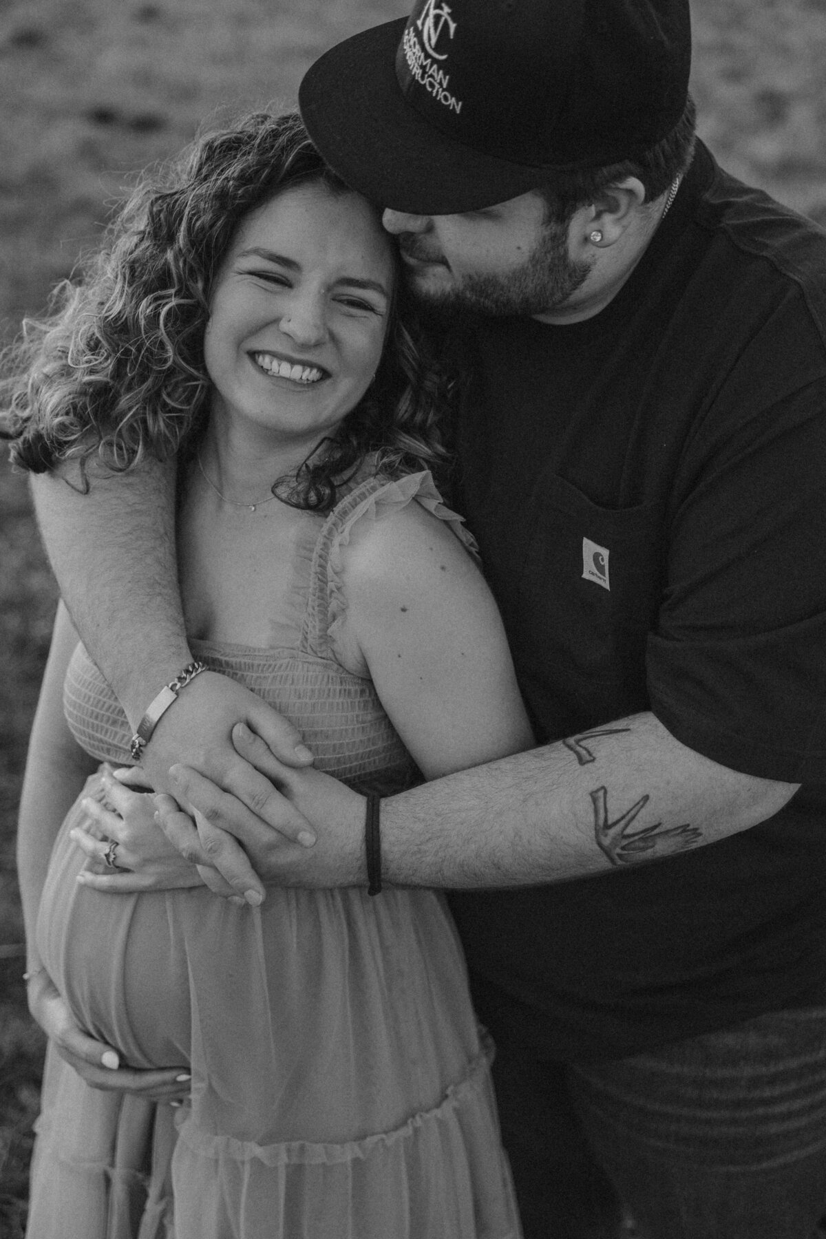 Joyful Black and White Maternity Photo of Expecting Couple Laughing and Embracing Outdoors