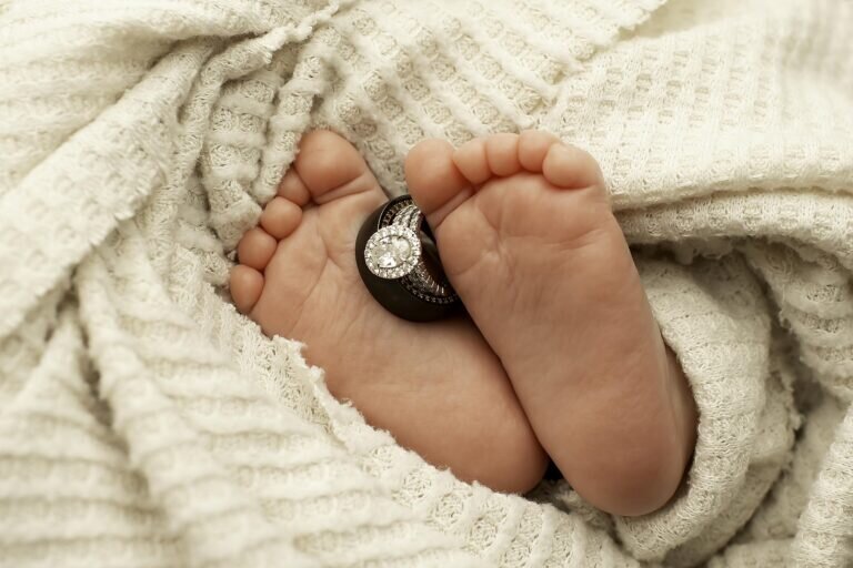 Close-up of tiny newborn feet with parents' wedding rings gently placed on the toes, symbolizing love, family, and a beautiful new beginning