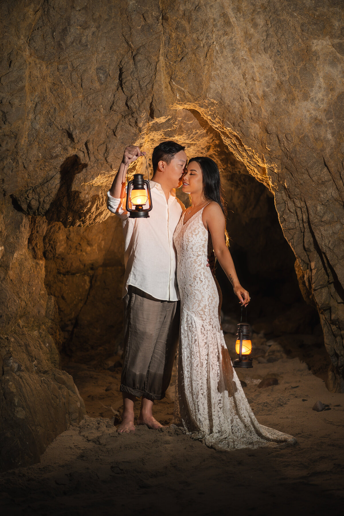 Asian couple eloping at El Matador State Beach in Malibu kissing in cave light glow holding lanterns.