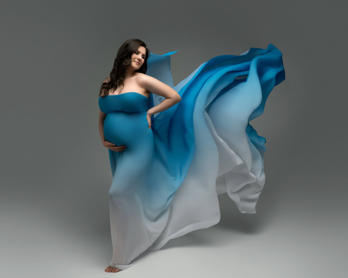 Studio maternity photo of a glowing mom-to-be in an ombré blue flowing gown, captured with motion and grace in Austin.