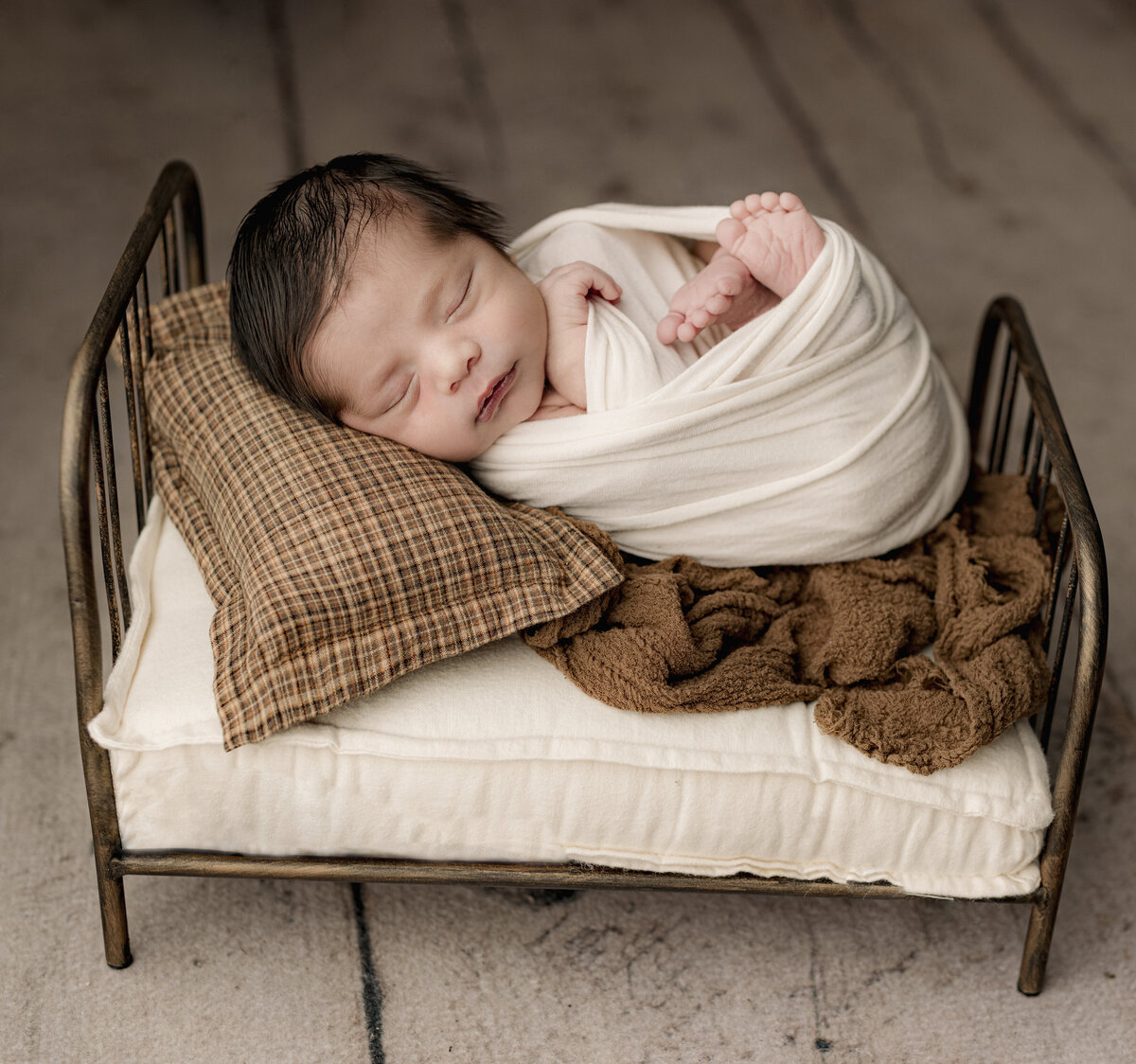 baby laying on small brown bed on wood backdrop