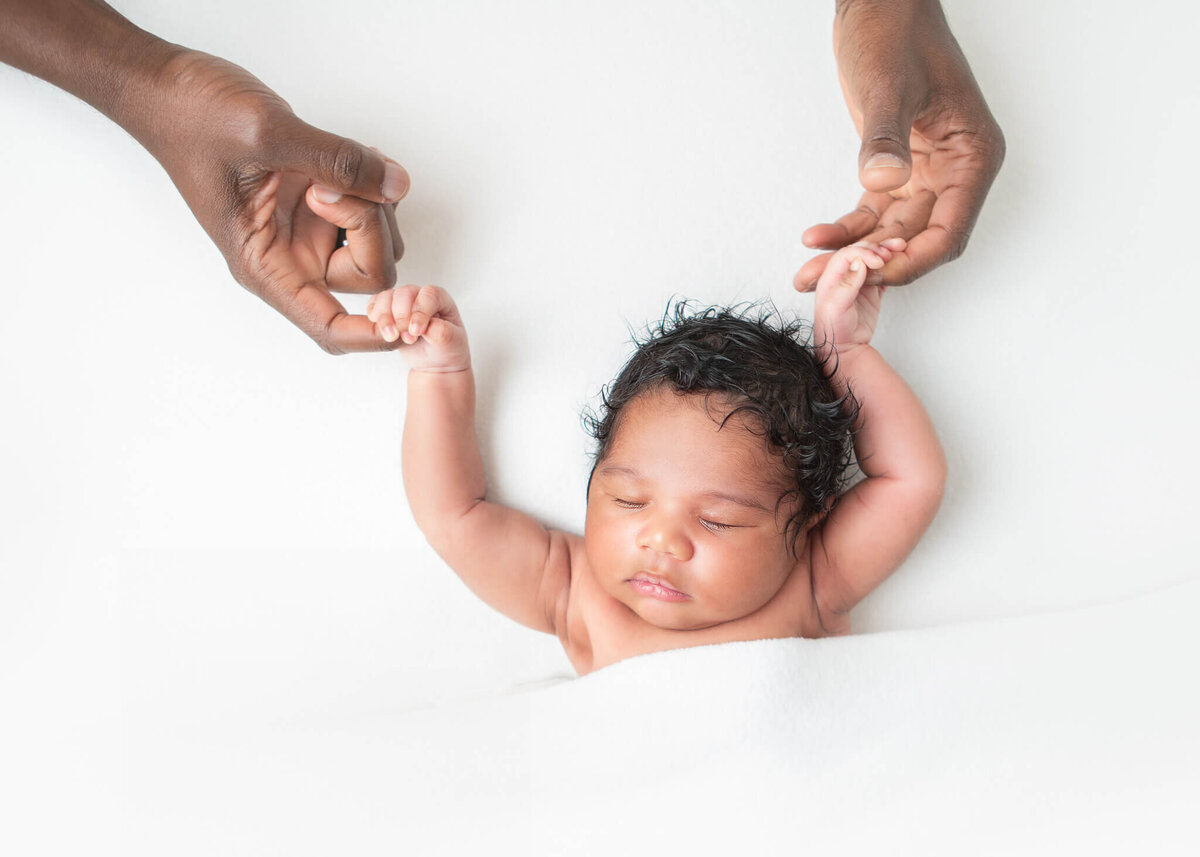 Newborn baby girl holding onto her dads hands captured by LA baby photographer
