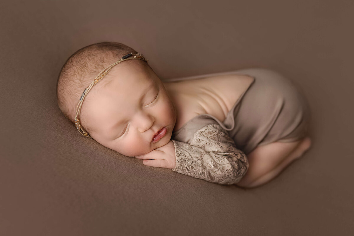 Newborn girl laying on brown blanket