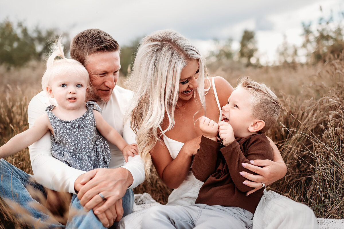 mom sitting with boy and dad holding baby girl while they sit in the grass