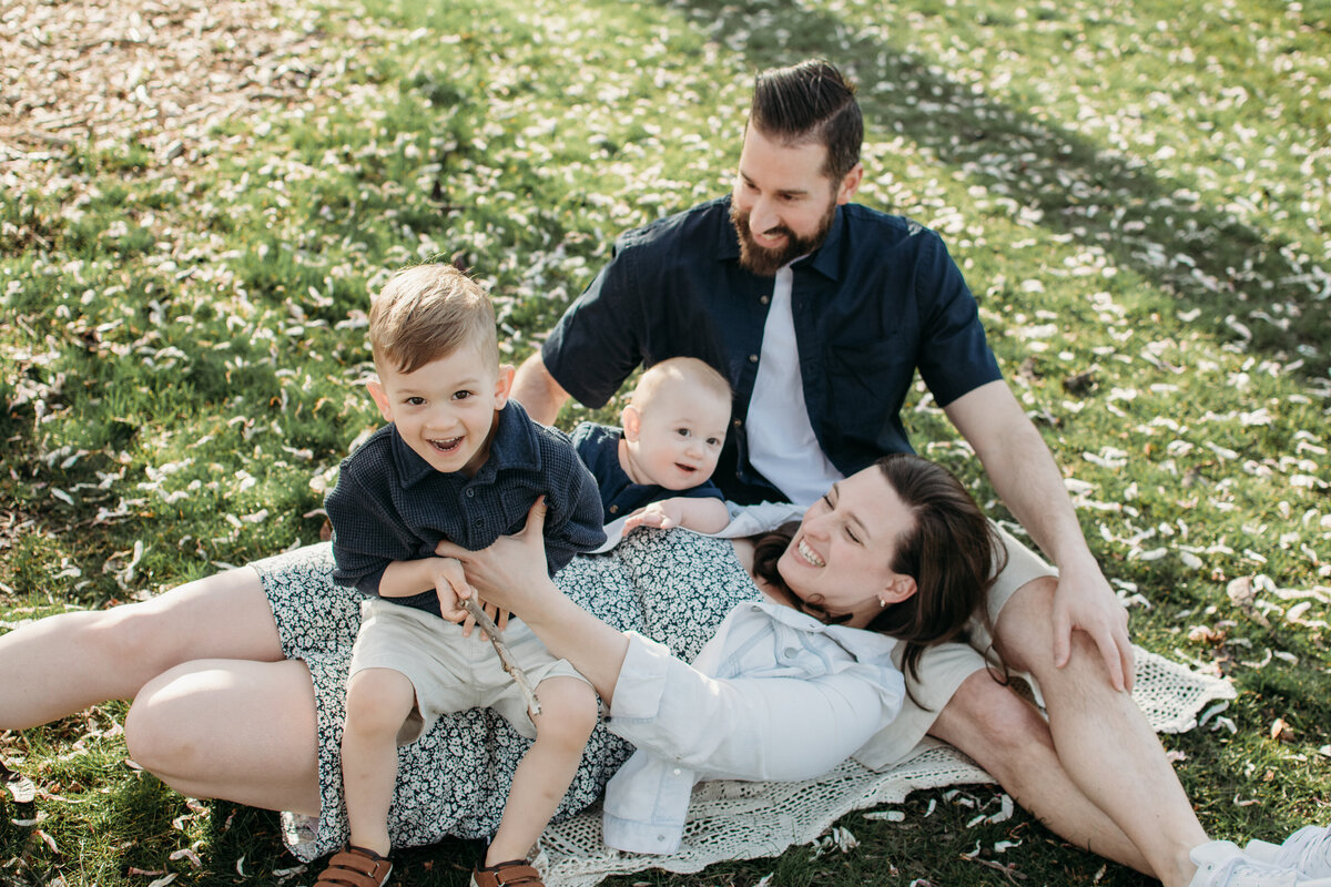 Family laying on the grass playing with their baby and toddler during a family photo session in Elmhurst, IL