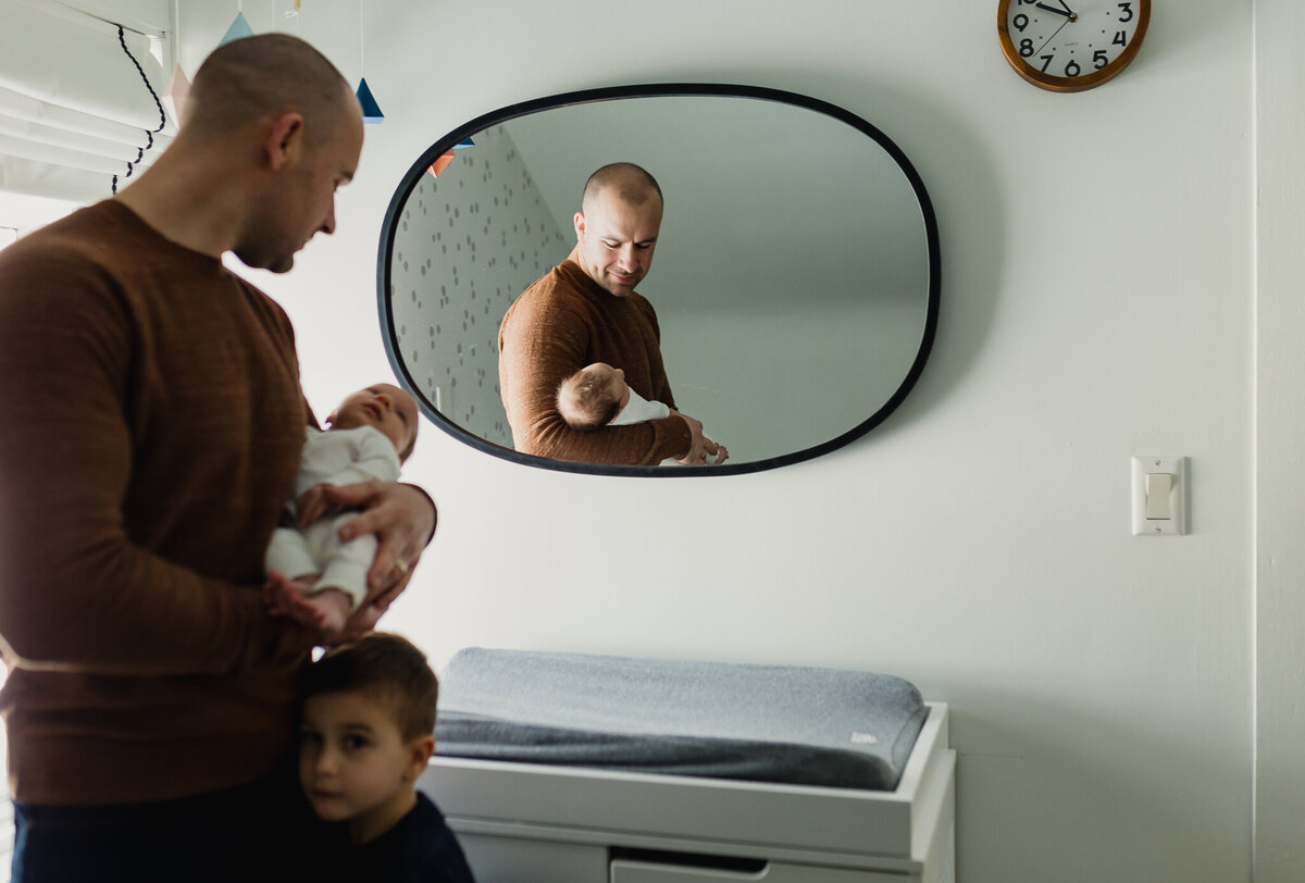 Family photo with a dad holds newborn with older son looking at camera