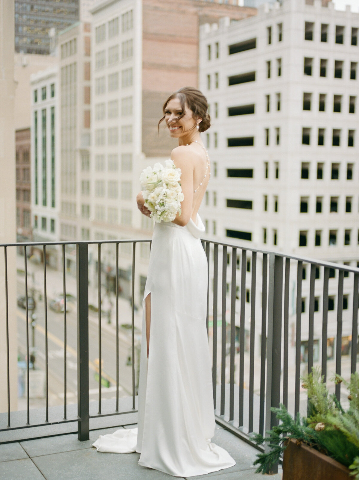 bride in backless pearl detail wedding dress with simple white bouquet on Shinola Hotel balcony
