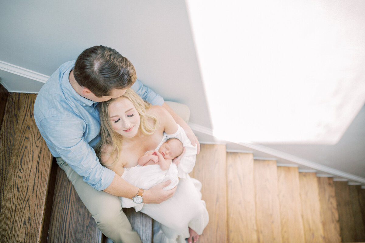 Blonde new mom holds her newborn while sitting with her husband on their wooden steps