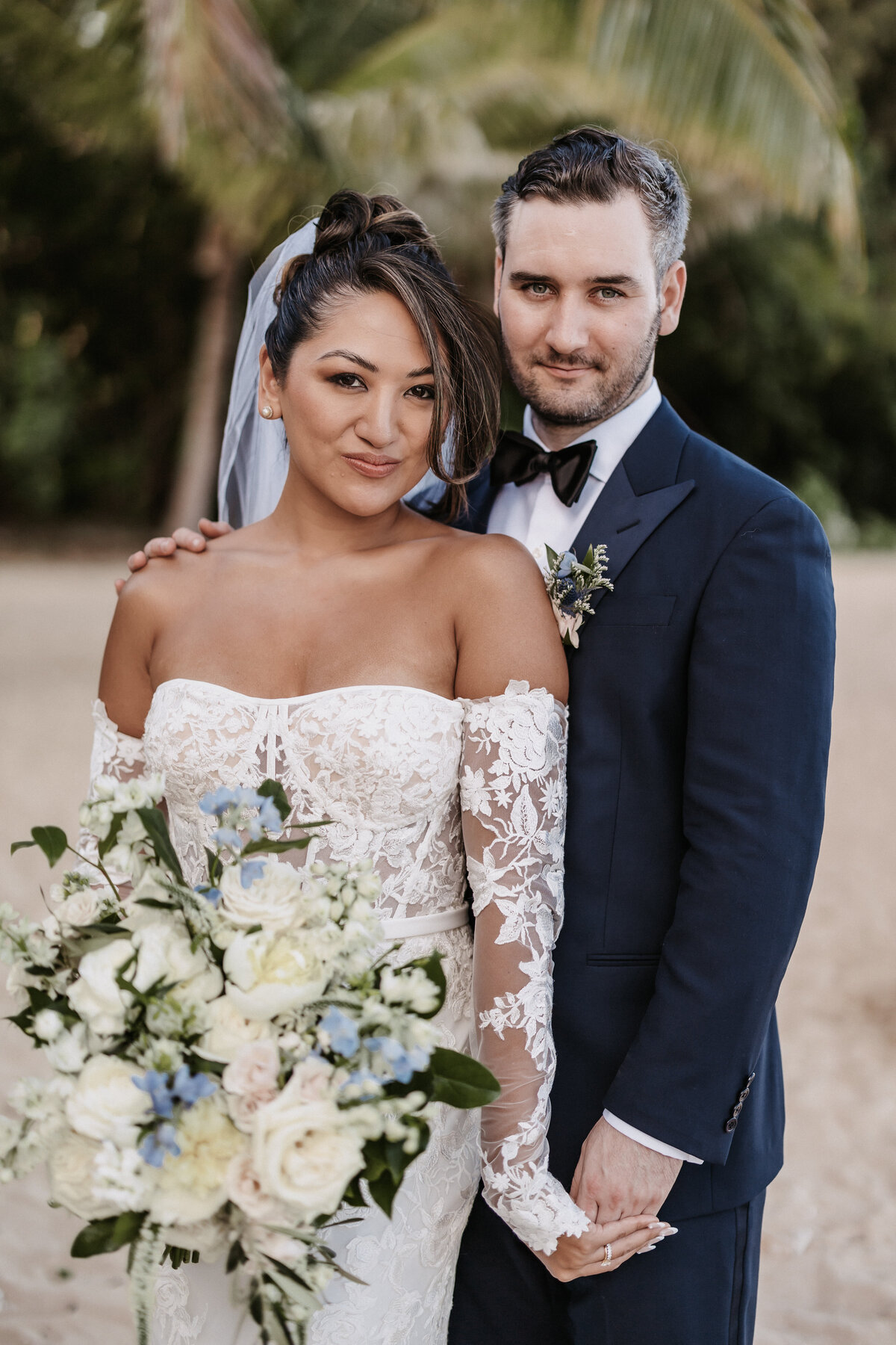 Wedding couple portrait holding hands standing with each other holding bouquet on the beach