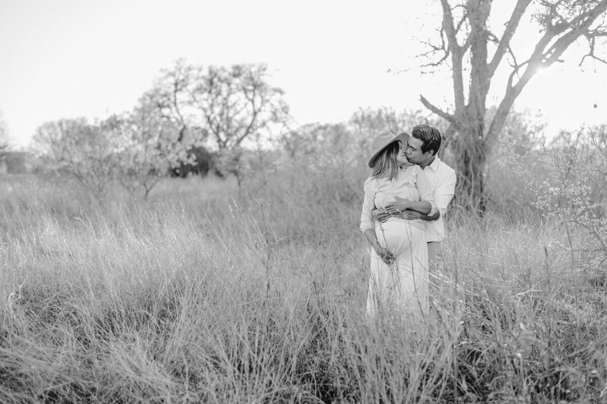 Black and white pull-back image of an expecting couple embracing.