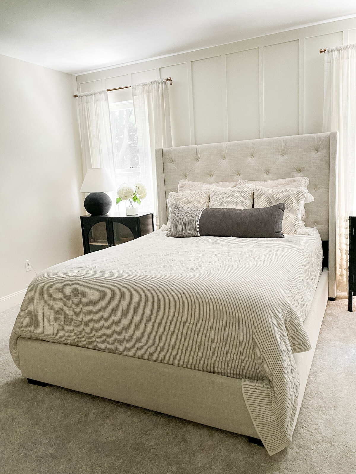 Master Bedroom upholstered  headboard with white curtains and black arched bedside tables