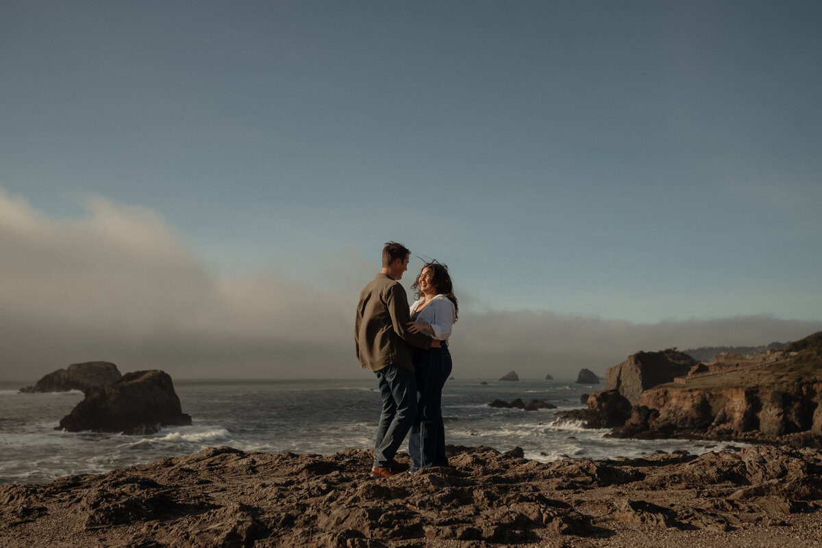 authentic, windswept moment of engaged couple laughing together on the sandy Oregon shoreline