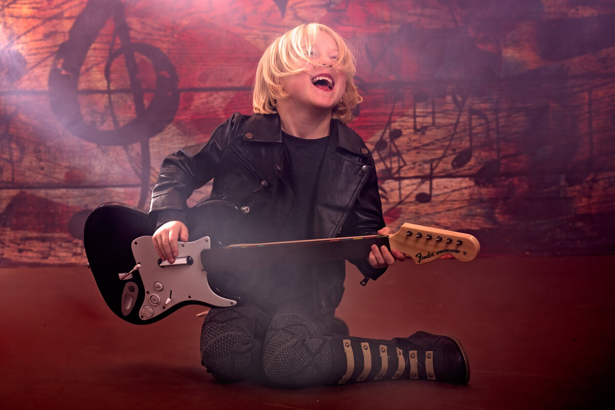 Dynamic portrait of a young child rocking out with an electric guitar, set against a dramatic stage backdrop. Captured in Overland Park, Kansas, this bold and creative setup is ideal for families seeking edgy and artistic child photography.