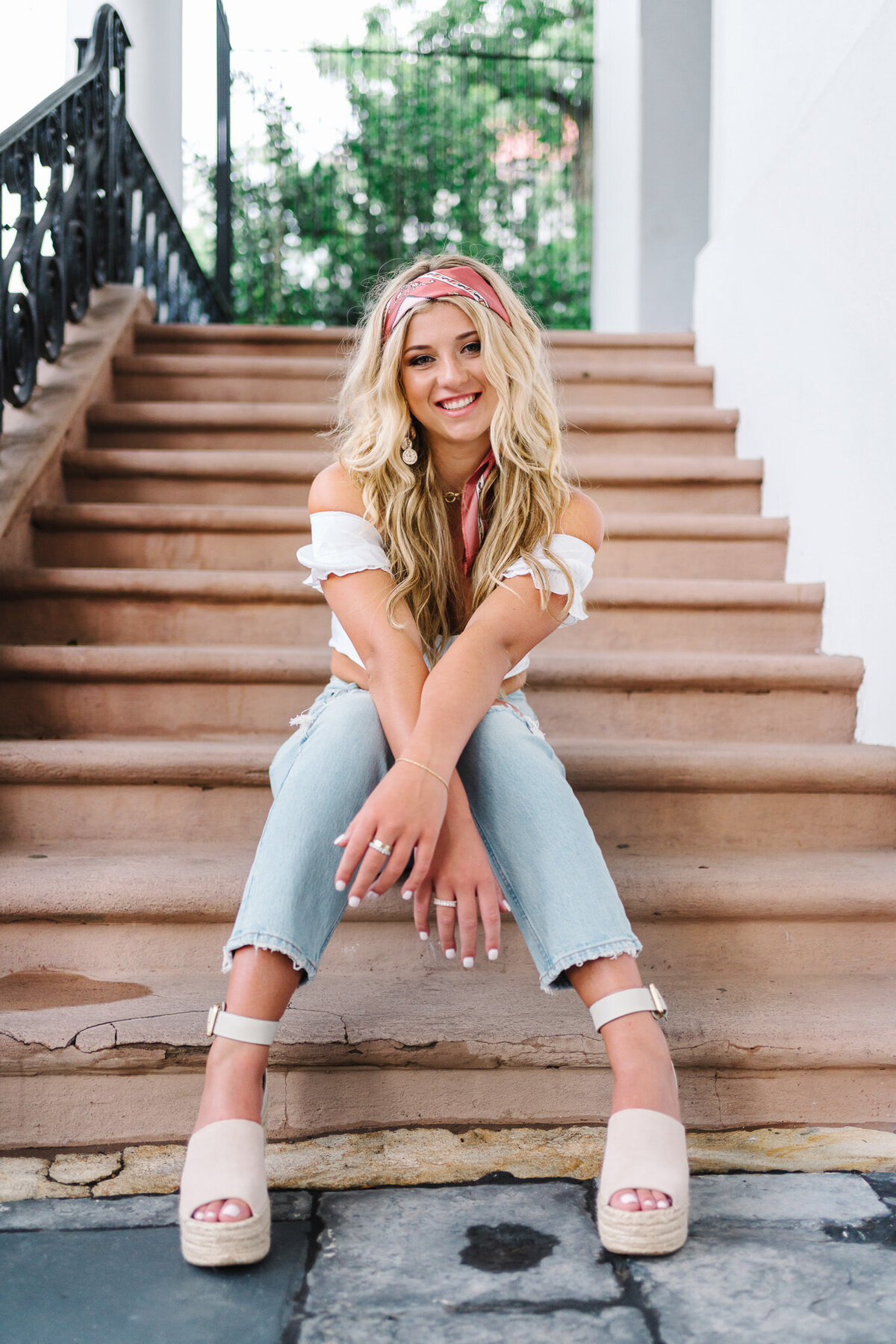 Senior girl sitting on staircase in blue top and jeans in downtown Charleston