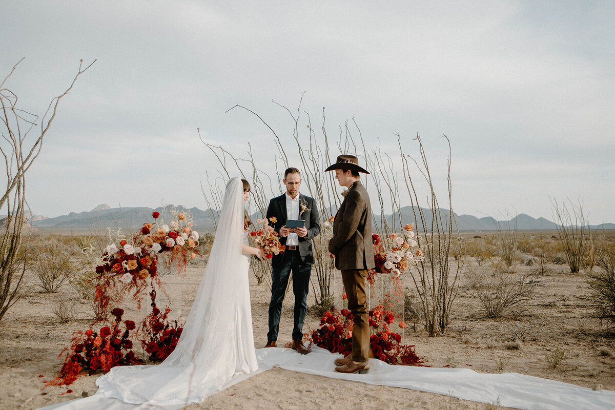 Two people getting married with an officiant in the desert of West Texas, surrounded by red and white flowers
