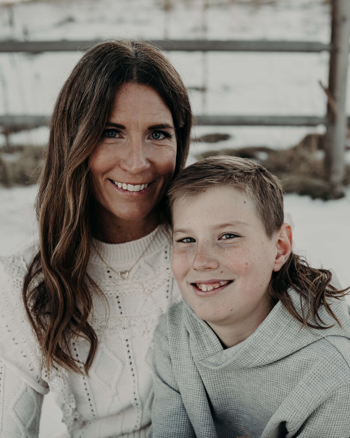 A beautiful portrait of a mother and son, smiling directly towards the lens during an outdoor winter photography session.