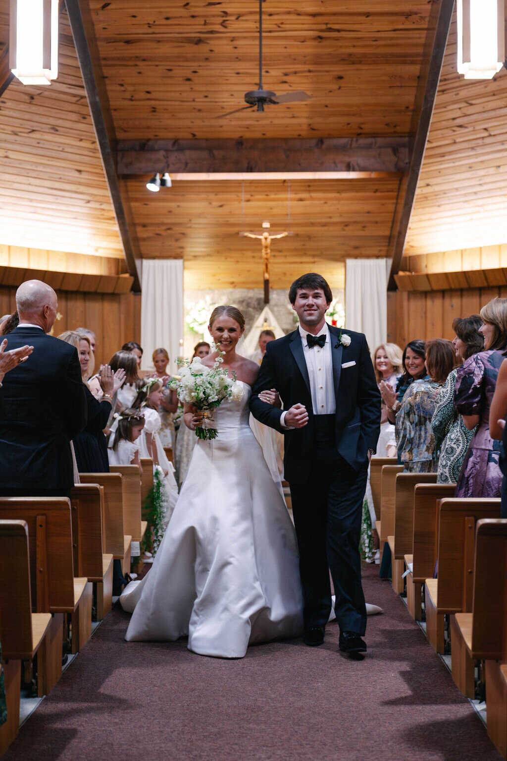 Bride and groom walking back up the aisle after their ceremony at a church wedding in Highlands, North Carolina, smiling as guests applaud.