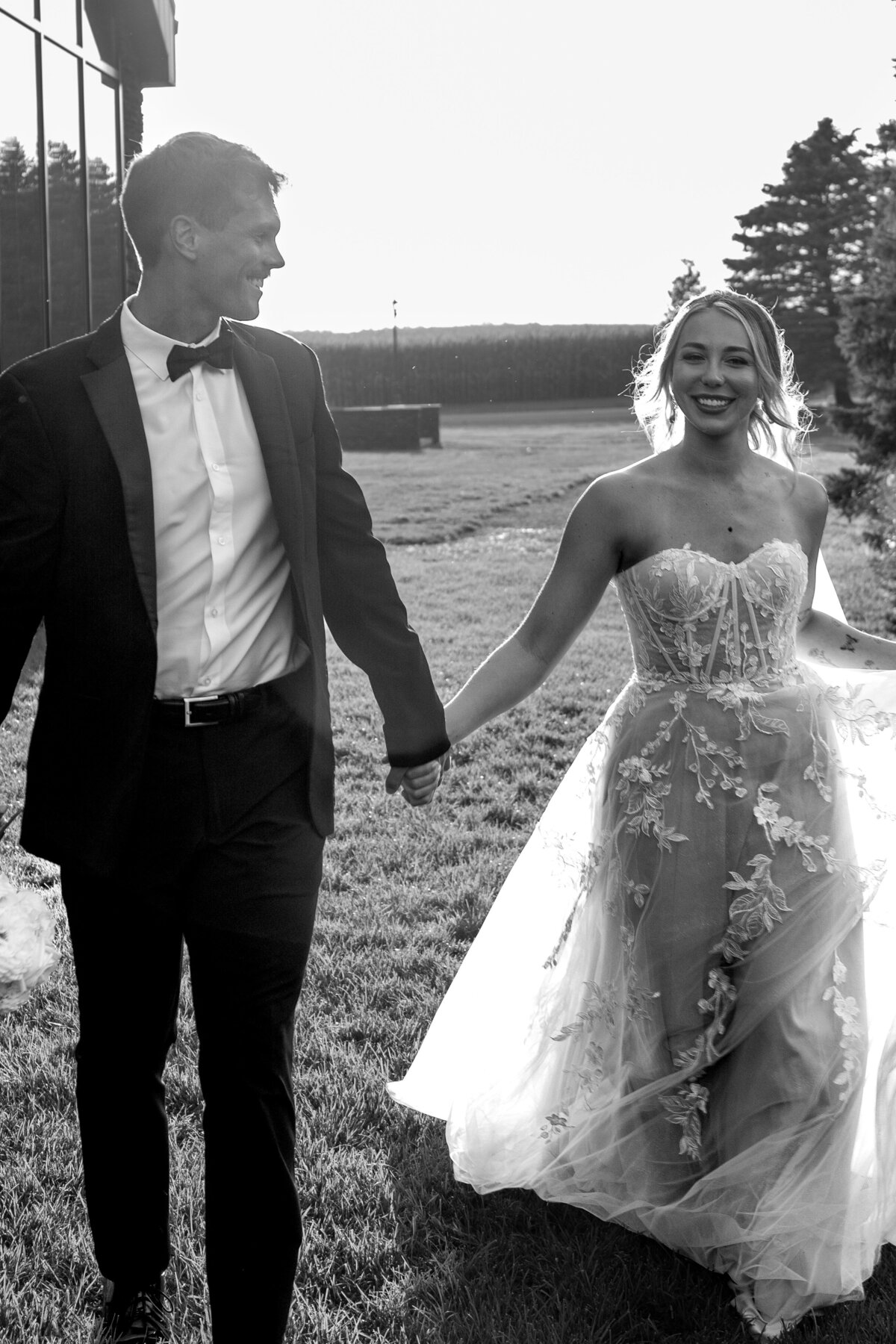 A black and white portrait of a bride and groom holding hands while they run through the grass; taken by columbus wedding photographer A James Visuals.