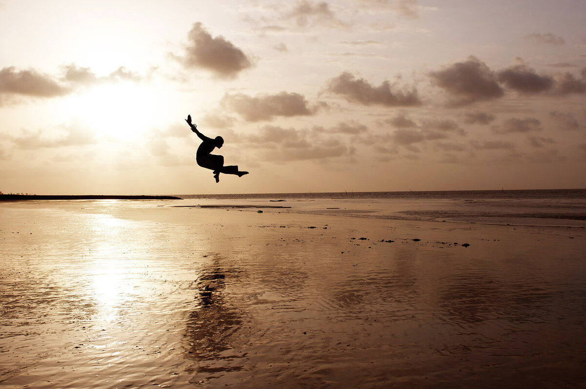 A person jumping up while dancing at sunset at the water's edge