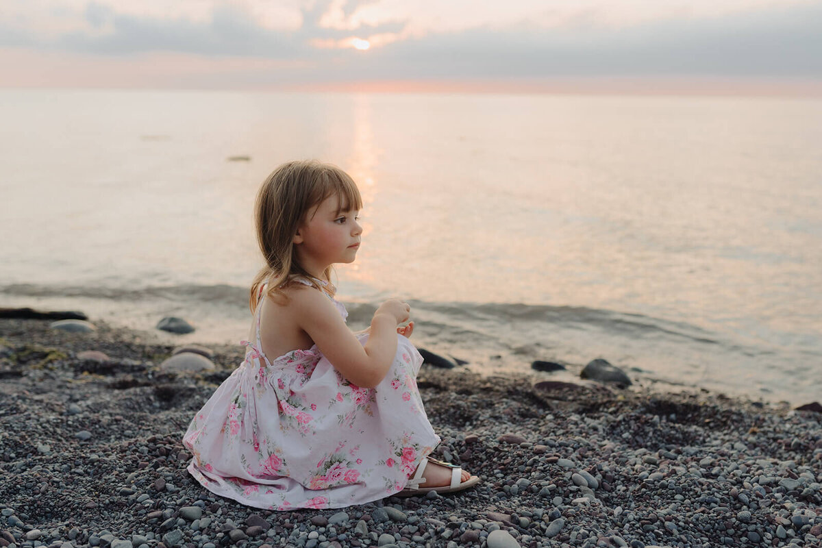 Young girl sitting by beach at family with two kids on the beach at family photo shoot in Finger Lakes, NY