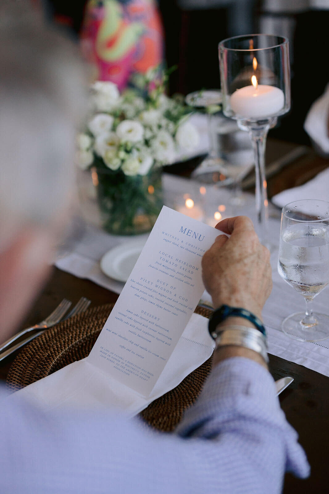 An old man is reading the menu at the dining table in a wedding reception at Cape Cod Summer Tent, MA.