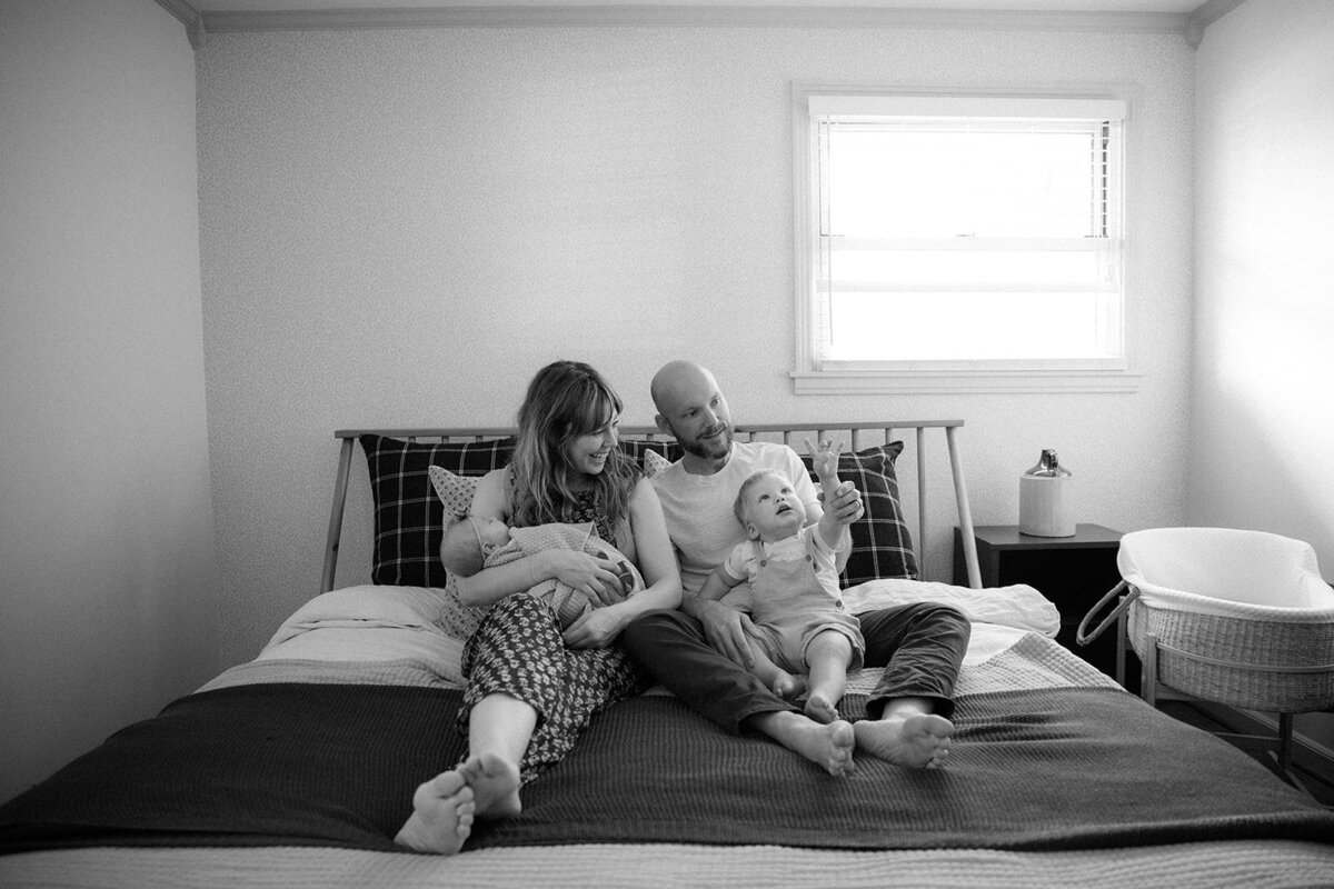 Family of four piles onto parents bed comfortably together for family time. 
