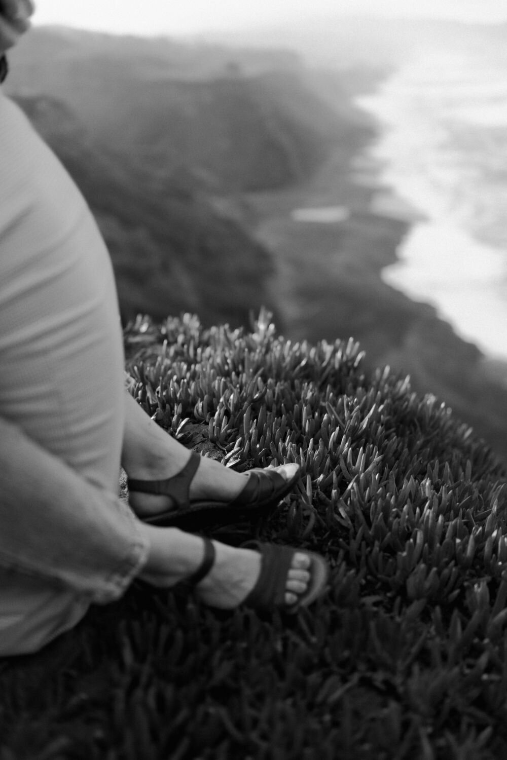 black and white photo of womans feet and heels on california coast cliff with ocean in background