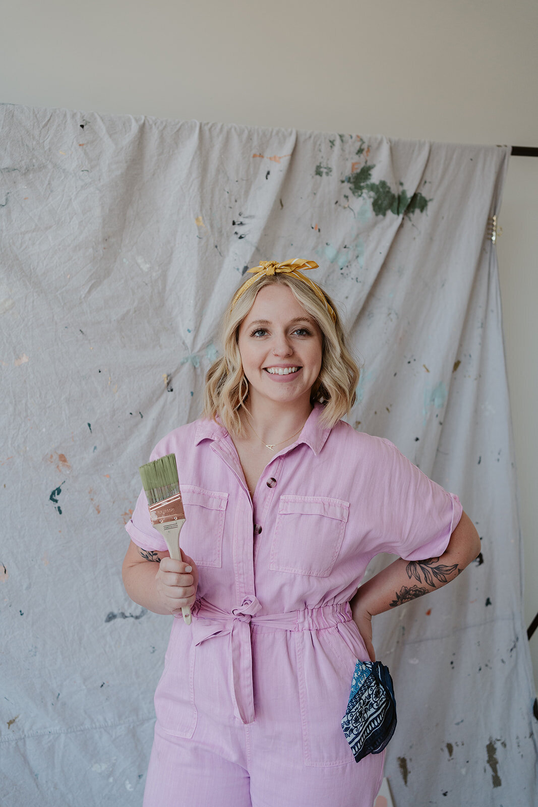Full-body portrait of an artist holding a paintbrush in a pink jumpsuit during a Wildher and Co studio branding session.