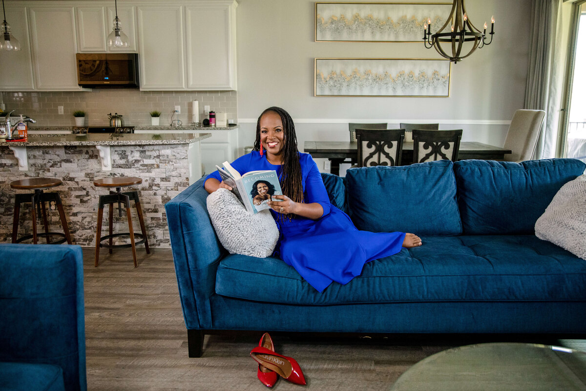 female author sitting on a blue couch in a living room holding her book and smiling