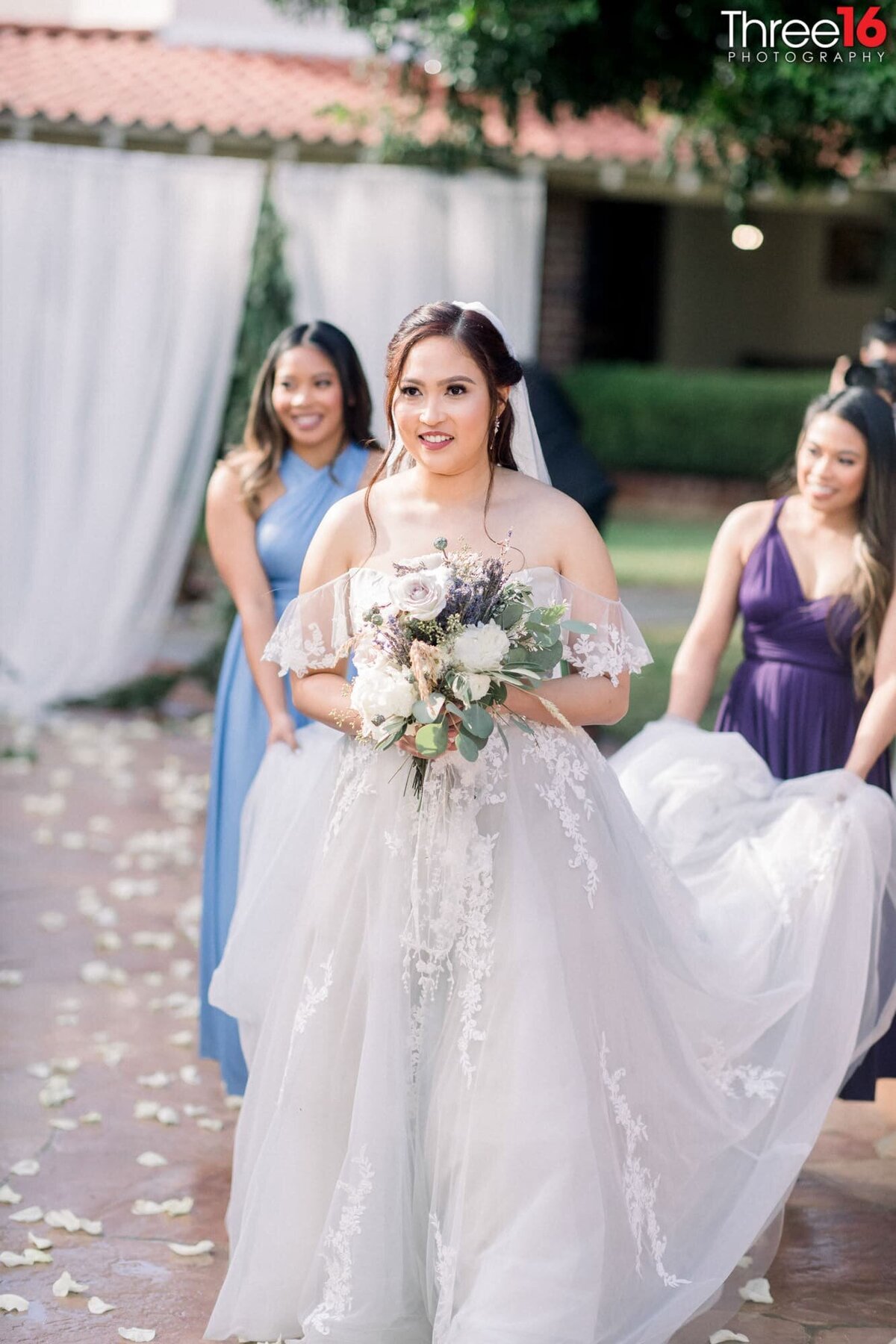 Bride enters as Bridesmaids carry her train so it doesn't drag in the dirt