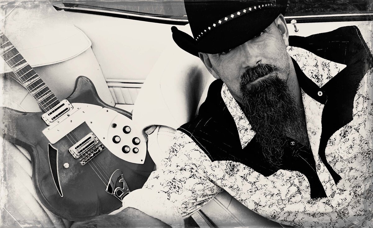 Male musician portrait black and white Todd Richard wearing black cowboy hat white cowboy shirt while sitting with electric guitar beside