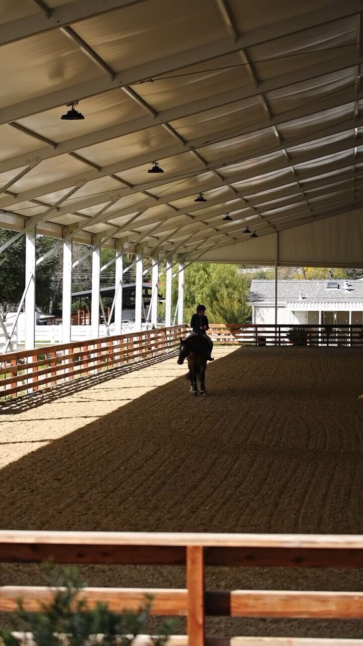 A lone rider is shown in the middle of a very large covered riding arena at Fox Hollow Equestrian center in Pleasanton, CA