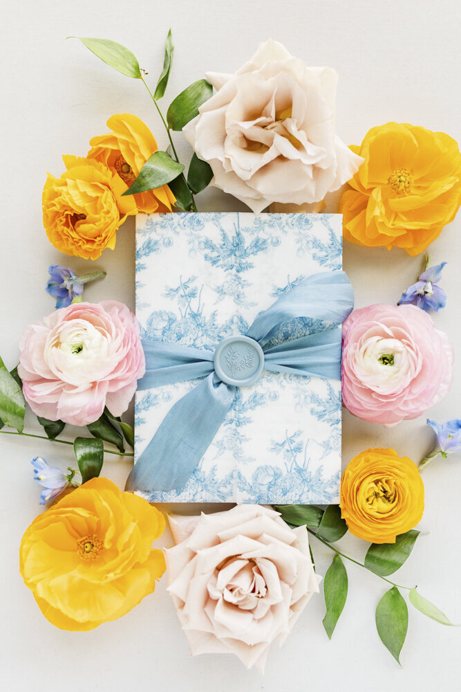 flat lay of blue wedding stationery surrounded by orange and pink flowers
