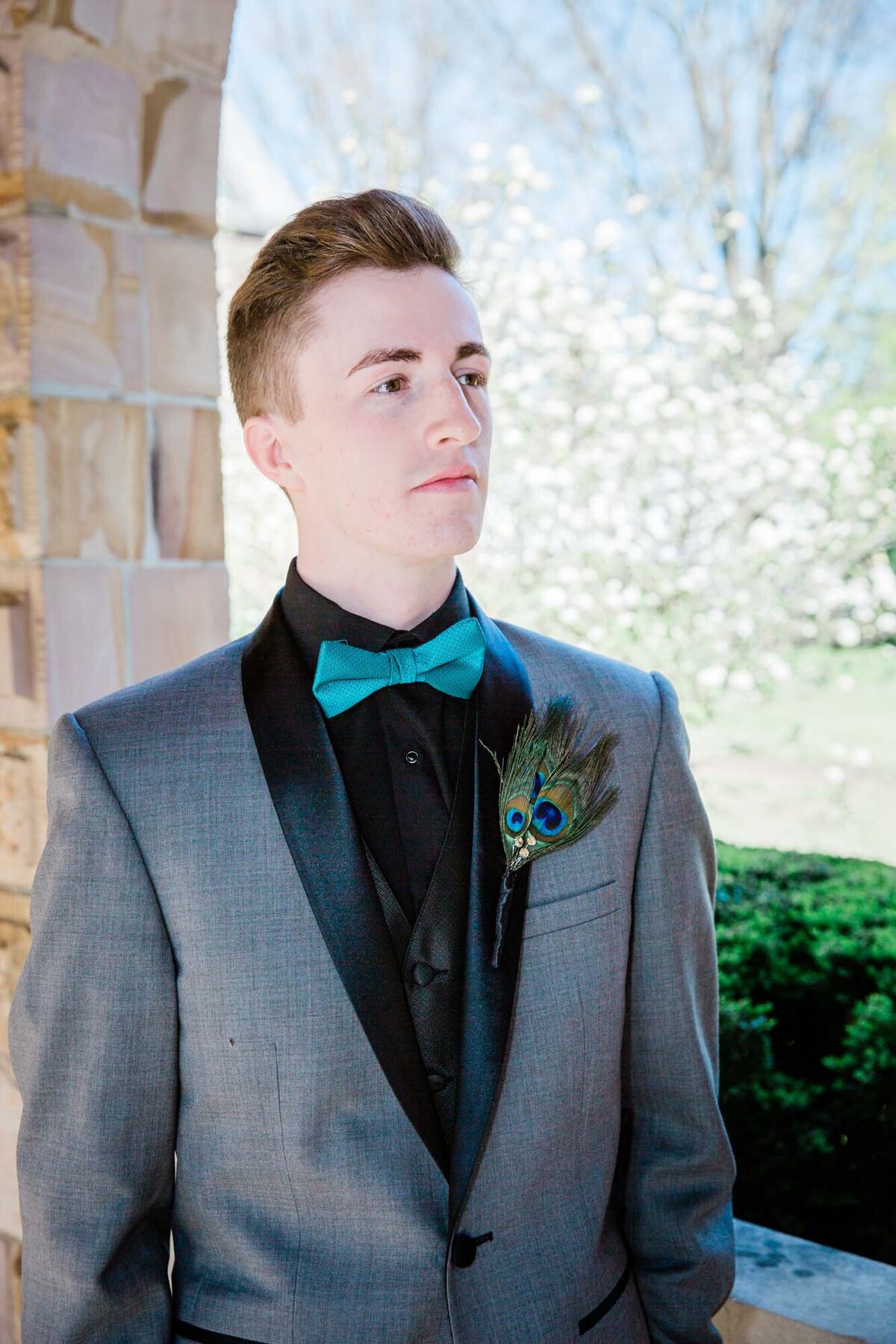 A dapper dude in his senior prom suit with beautiful flowering trees behind him.
