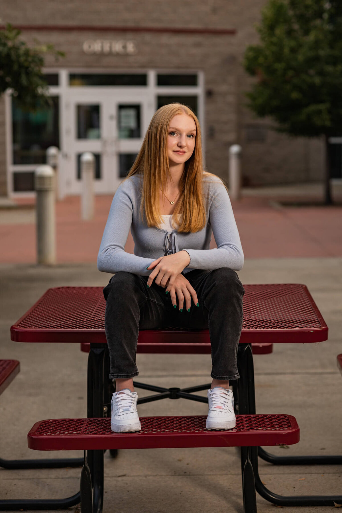 high school senior girl sitting on a picnic table in front of her high school