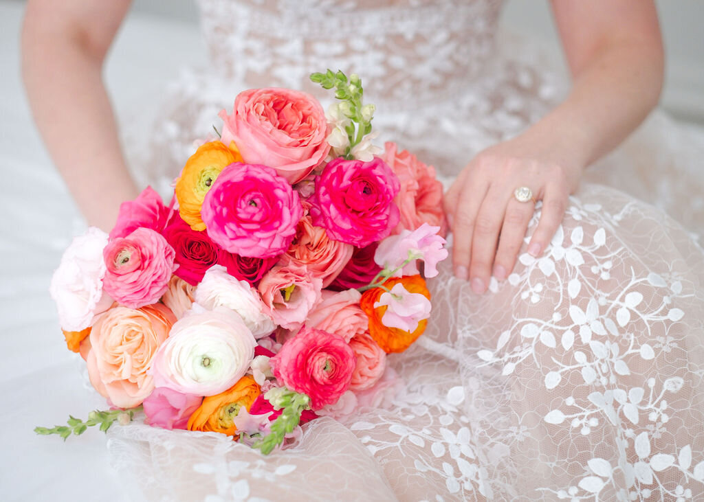 bride holding a romantic bouquet of bold pink and peach ranunculus flowers while wearing a delicate lace gown