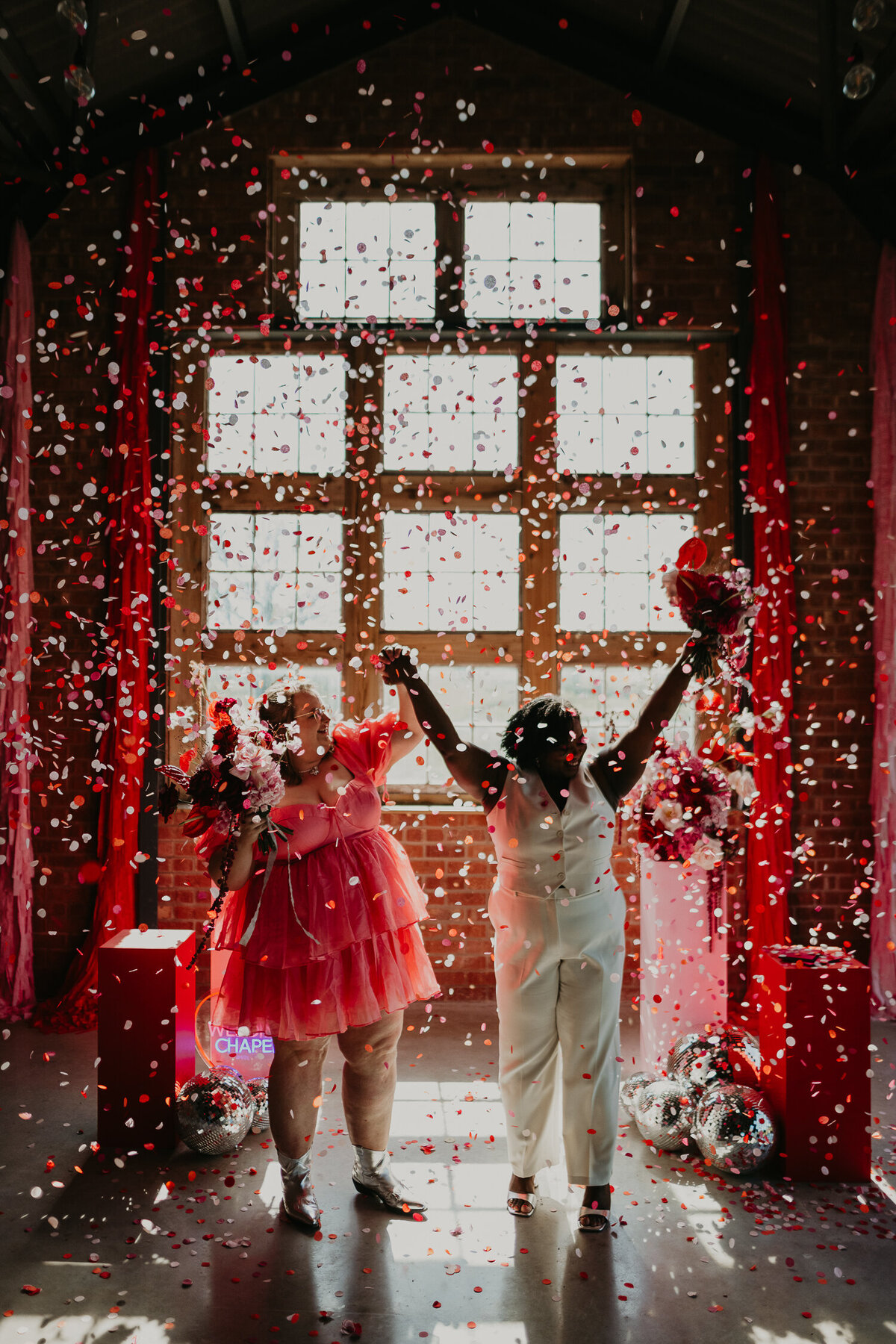 Same sex couple celebrate whilst being showered in pink and red confetti at The Giraffe Shed. 